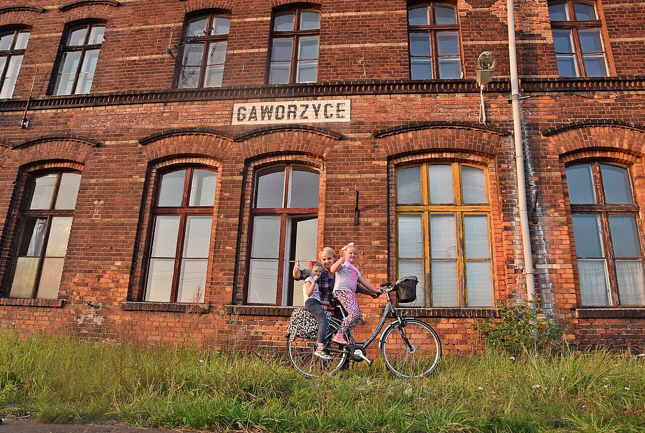 Na zdjęciu budynek dworca kolejowego w Gaworzycach. Przed nim na rowerze mama z córką.