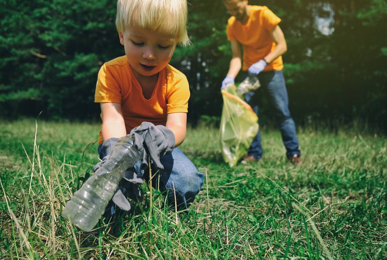 Na przykładowym zdjęciu widać dzieci w pomarańczowych koszulkach zbierające śmieci w parku.