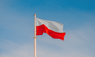 Zdjęcie przedstawiające biało-czerwoną polską flagę na maszcie na tle błękitnego nieba.
