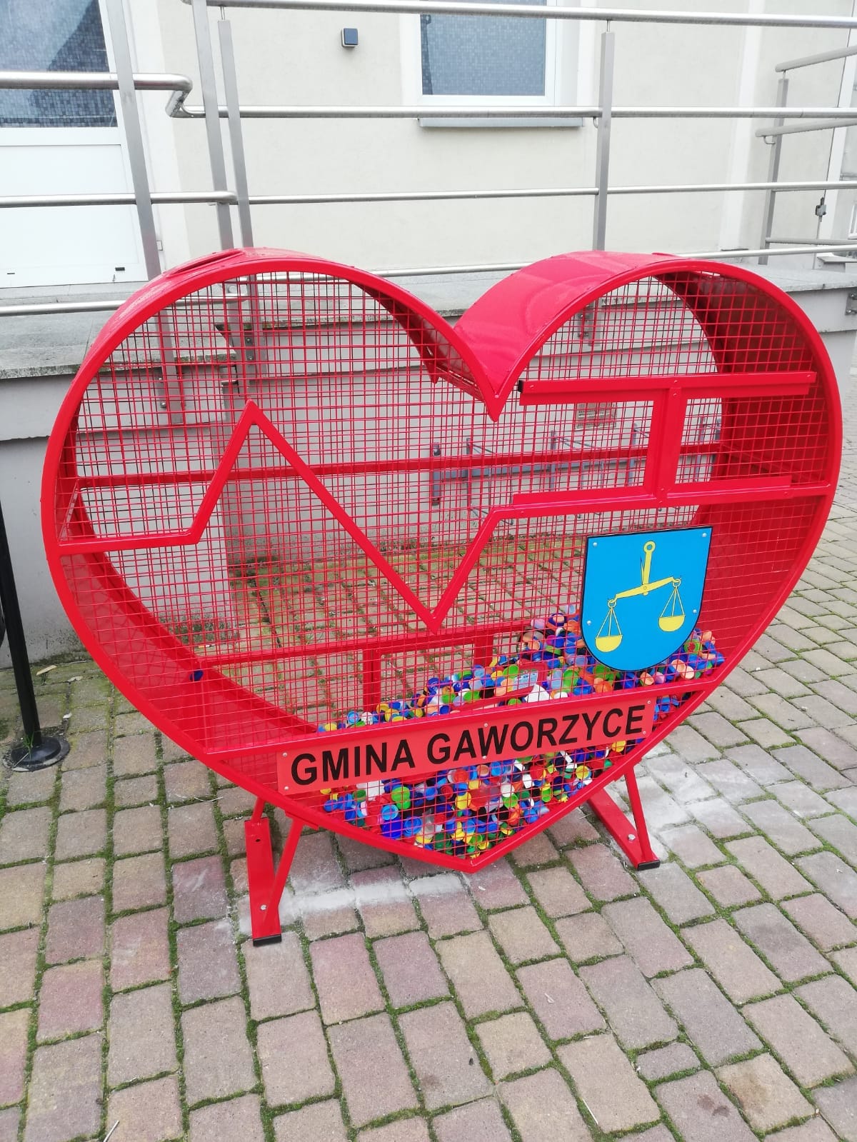 Zdjęcie metalowego, czerwonego serca na nakrętki zrobione pod siebią ośrodka pomocy społecznej w Gaworzycach.